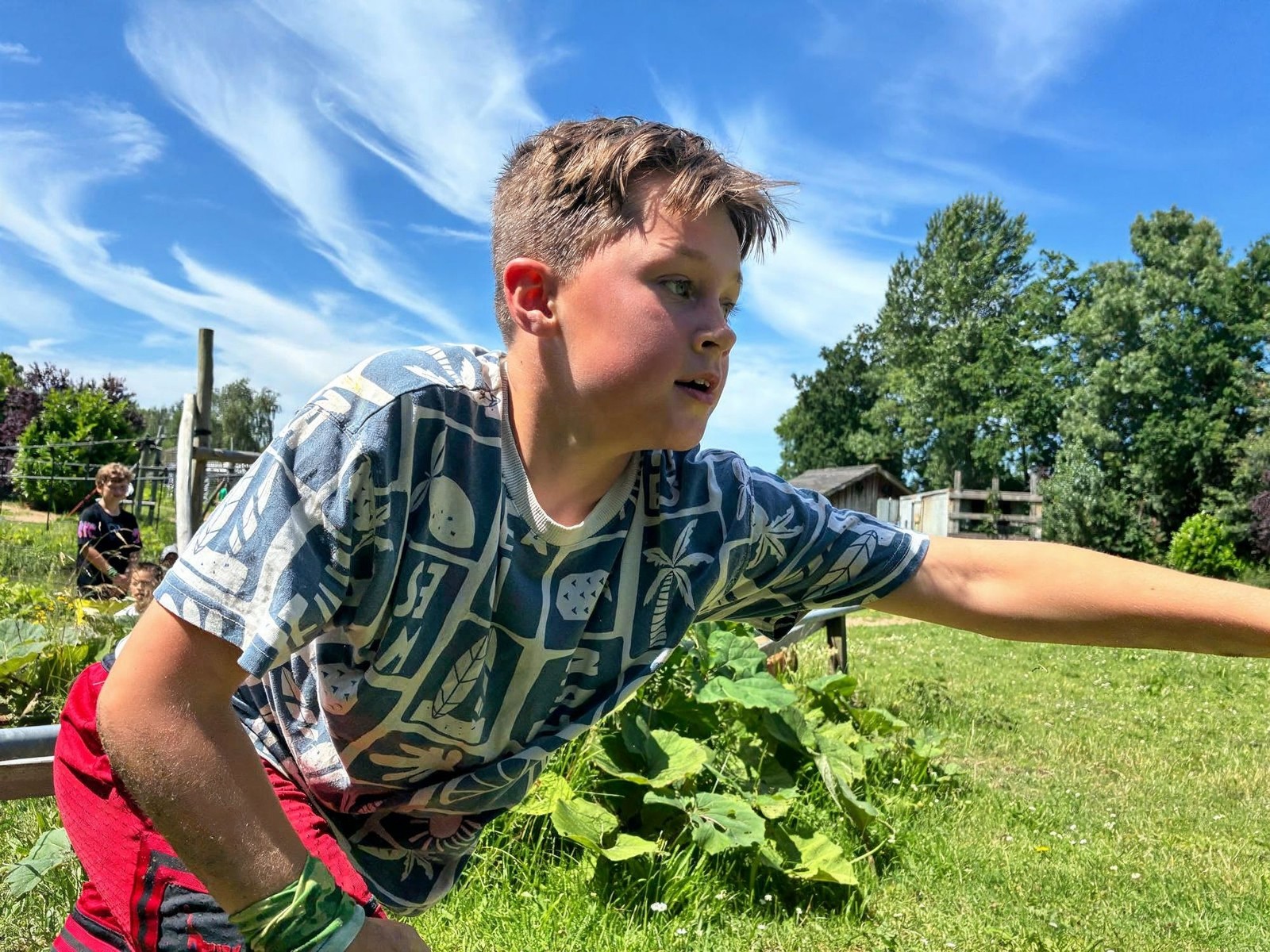 Kind in geruit shirt en rode broek balanceert op klimobstakel in buitenlucht met gras
