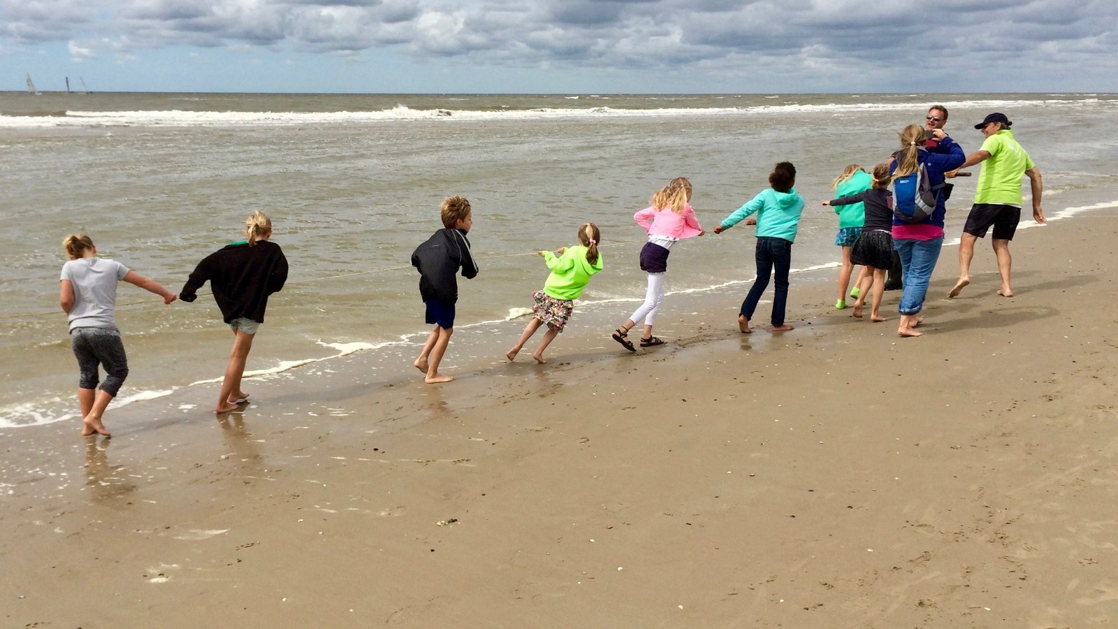 Groep kinderen loopt hand in hand het water in op een zandstrand met golven