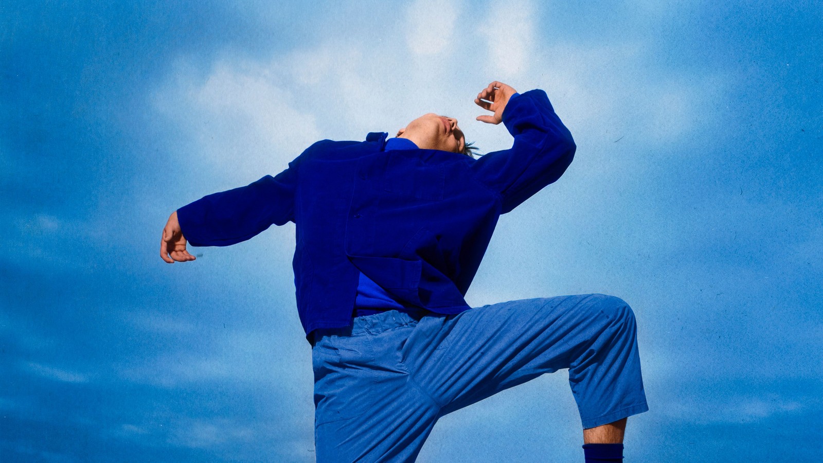 Theaterbeeld bij De lente vatte vlam: persoon in blauwe kleding met opgeheven knie tegen een blauwe lucht.