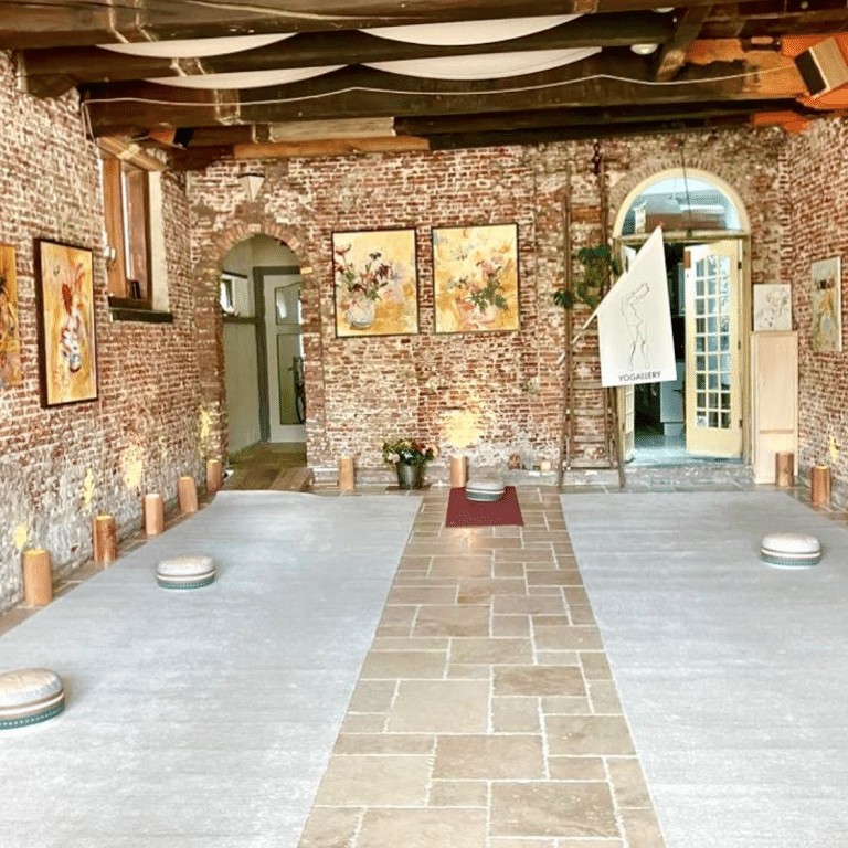 Interieur van expositieruimte Yogallery met bakstenen muren, twee deuren met groene en witte frames, schilderijen aan de wand, houten balken